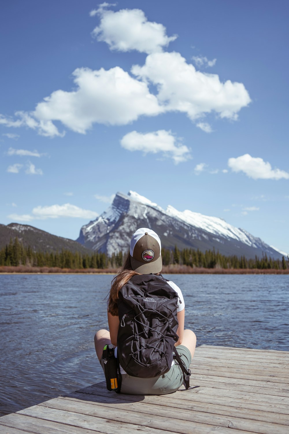 person in black and white backpack sitting on white wooden dock during daytime