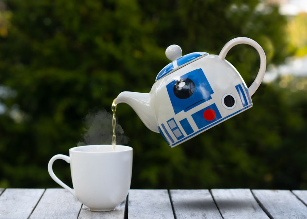 white blue and red ceramic teapot pouring water on white ceramic teacup