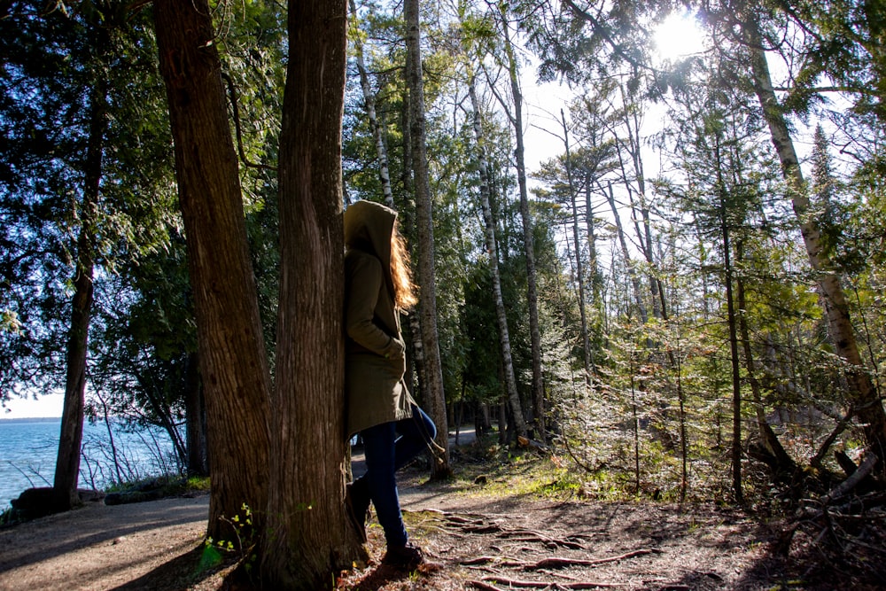 Mujer en chaqueta verde y pantalones negros caminando en el bosque durante el día