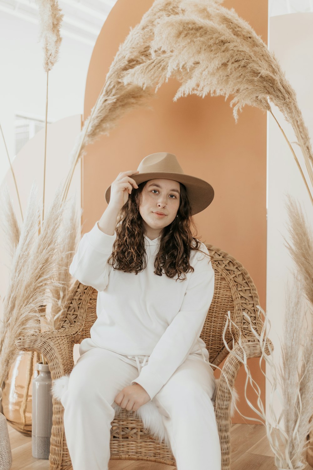 woman in white long sleeve shirt and white pants sitting on brown wicker chair