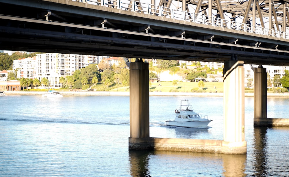 white and black motor boat on body of water under bridge during daytime