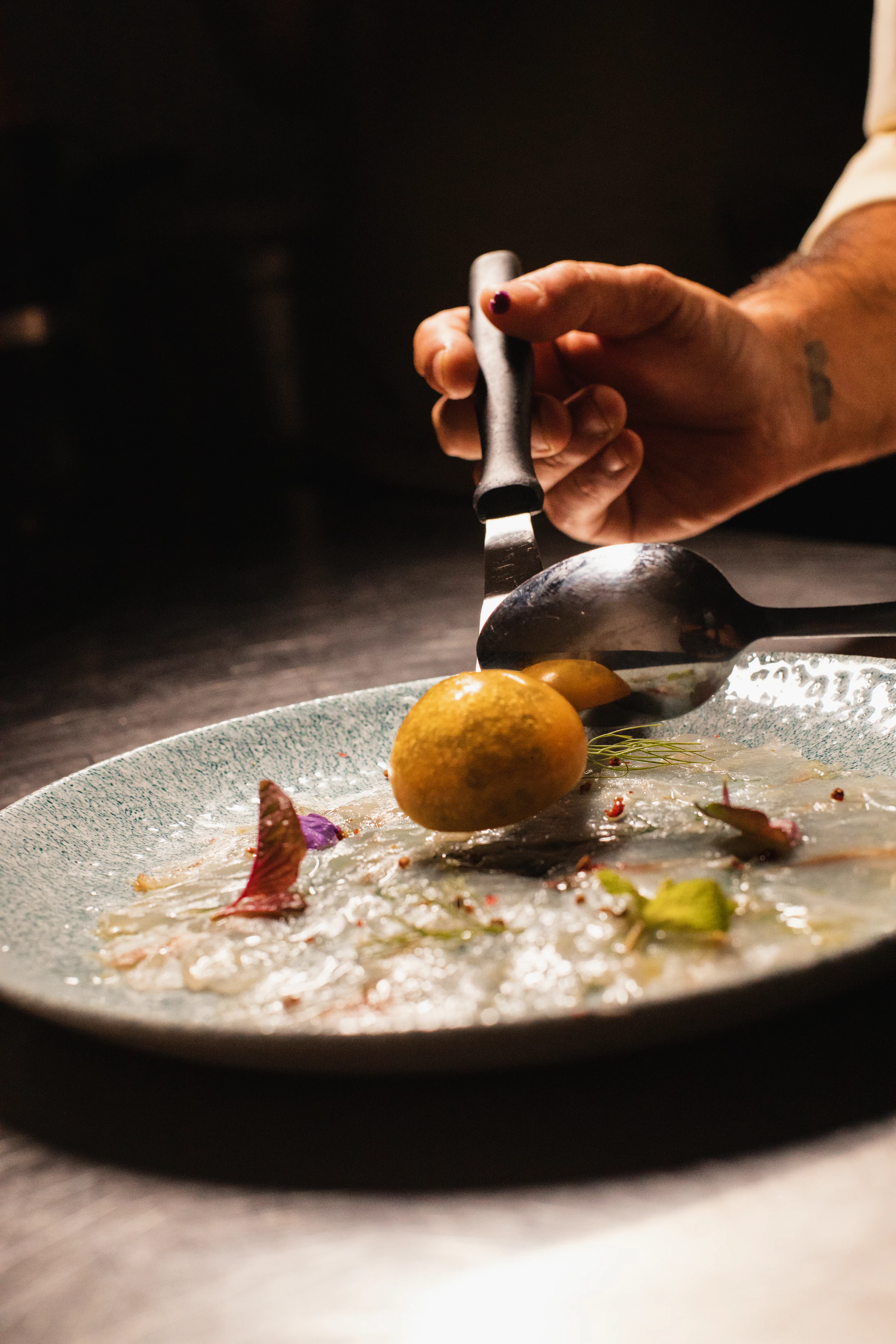 A cook's hands finishing a plate at the pass, steam rising in warm light