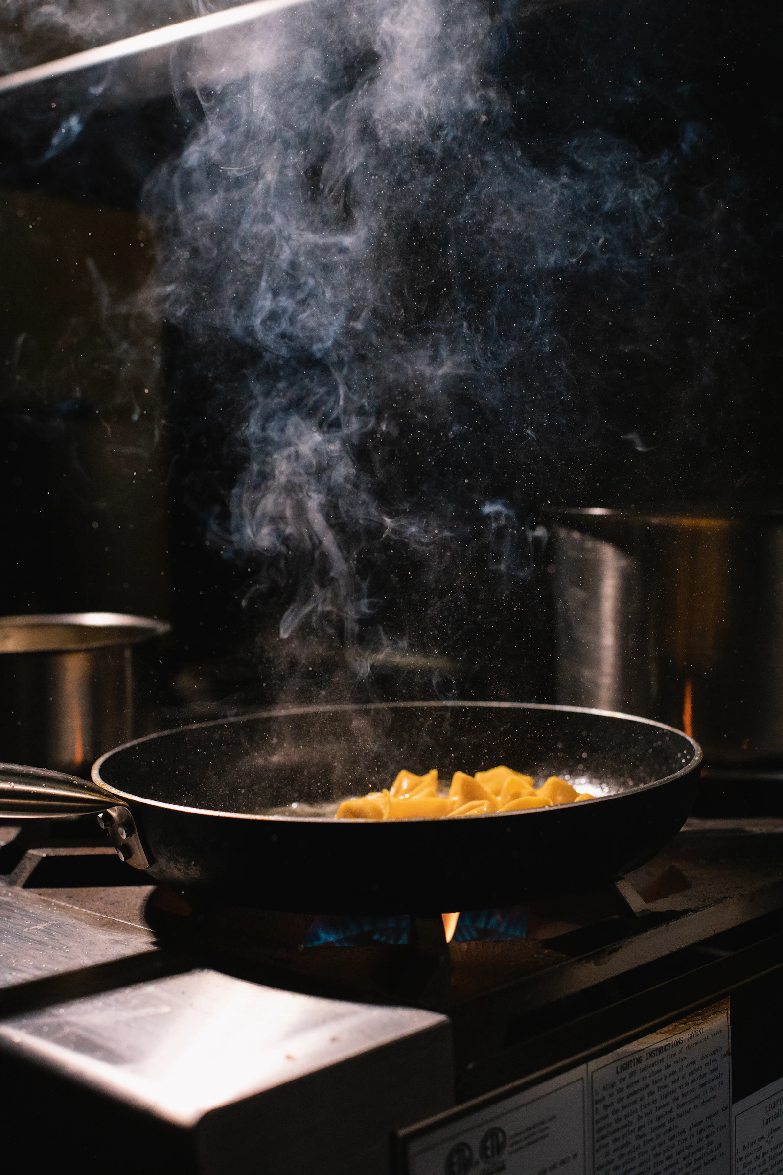 Black frying pan on a stove with smoke rising into darkness