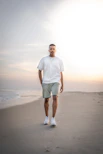 man in white crew neck t-shirt and green shorts standing on beach during daytime
