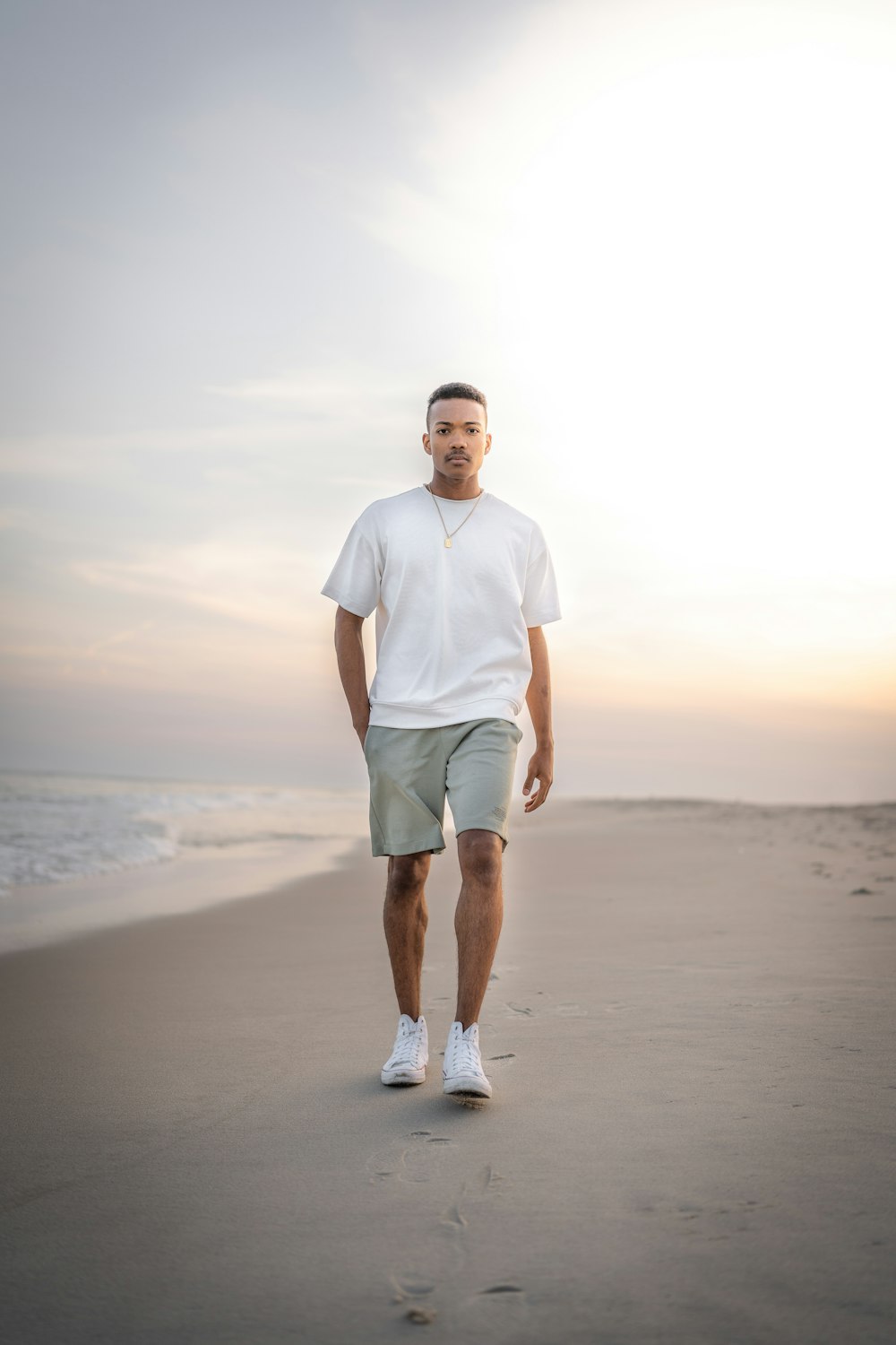 man in white crew neck t-shirt and green shorts standing on beach during daytime