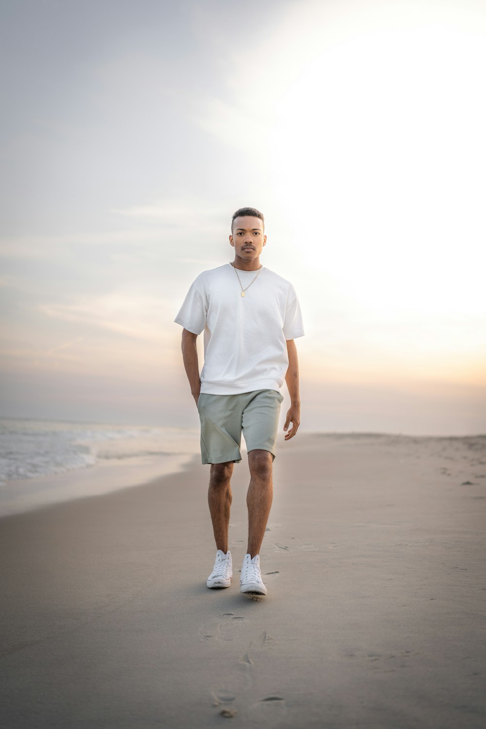 흰색 크루넥 티셔츠와 녹색 반바지를 입은 남자가 낮 동안 해변에 서 있다
