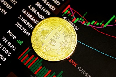 A gold Bitcoin coin resting on a digital display of financial market data, showcasing various stock tickers, charts, and numerical indicators.