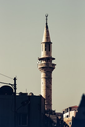 A tall, slender minaret with a pointed top and crescent moon finial rises above a structure with satellite dishes and antennas. The sky is clear and unobtrusive, providing a muted backdrop.