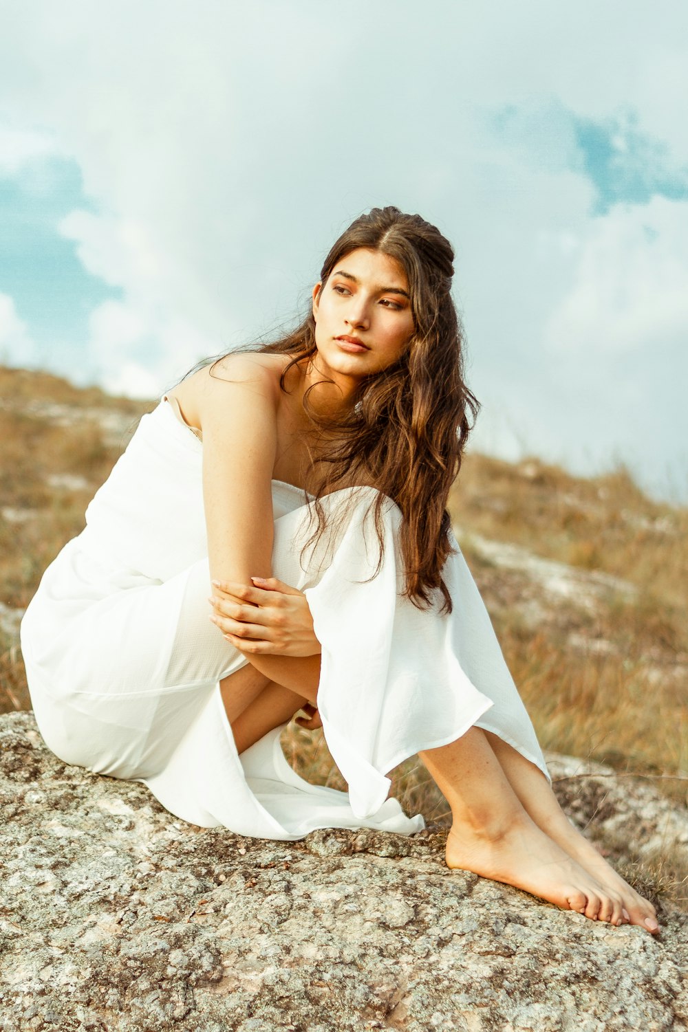 woman in white sleeveless dress sitting on brown rock during daytime