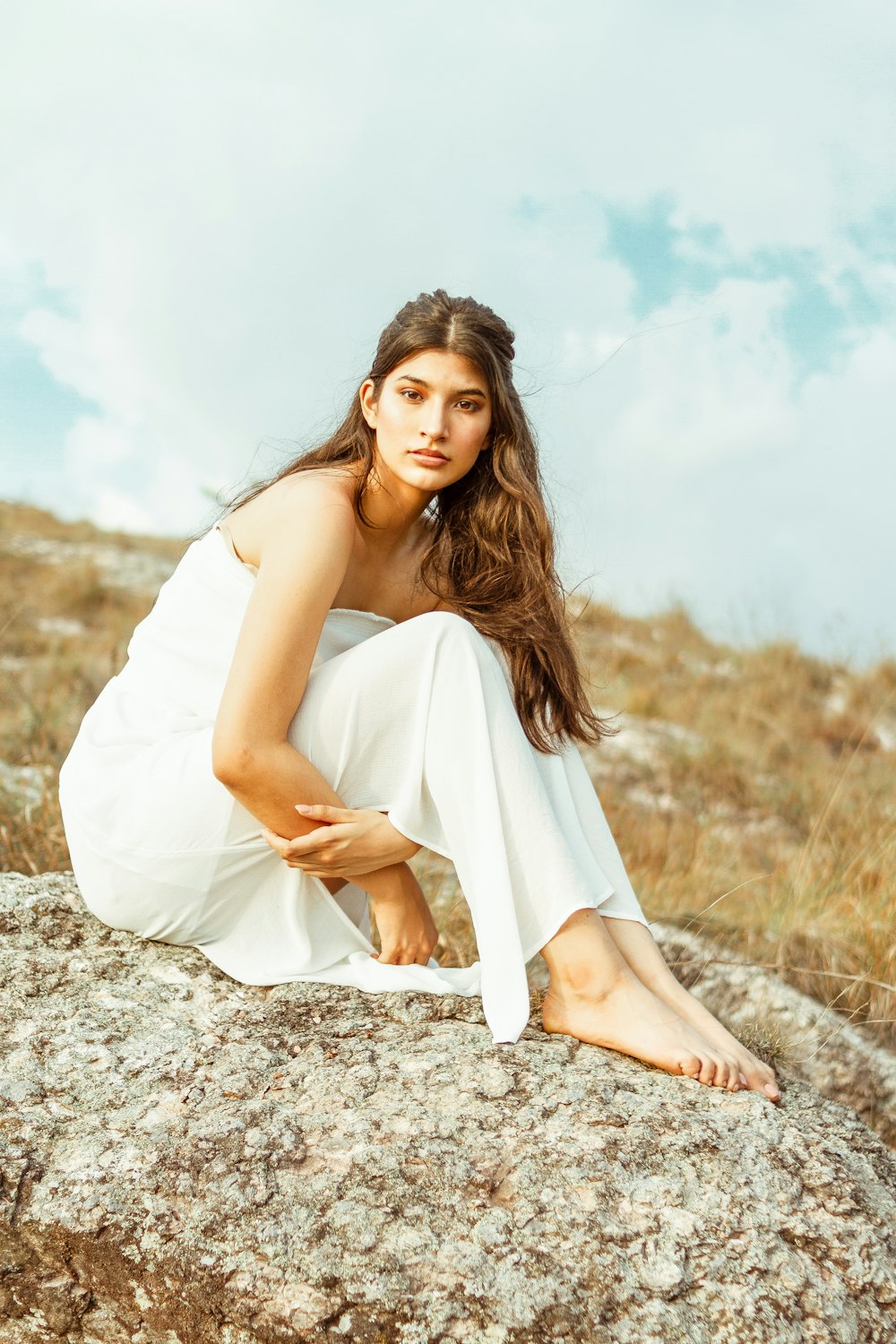 woman in white sleeveless dress sitting on brown rock during daytime