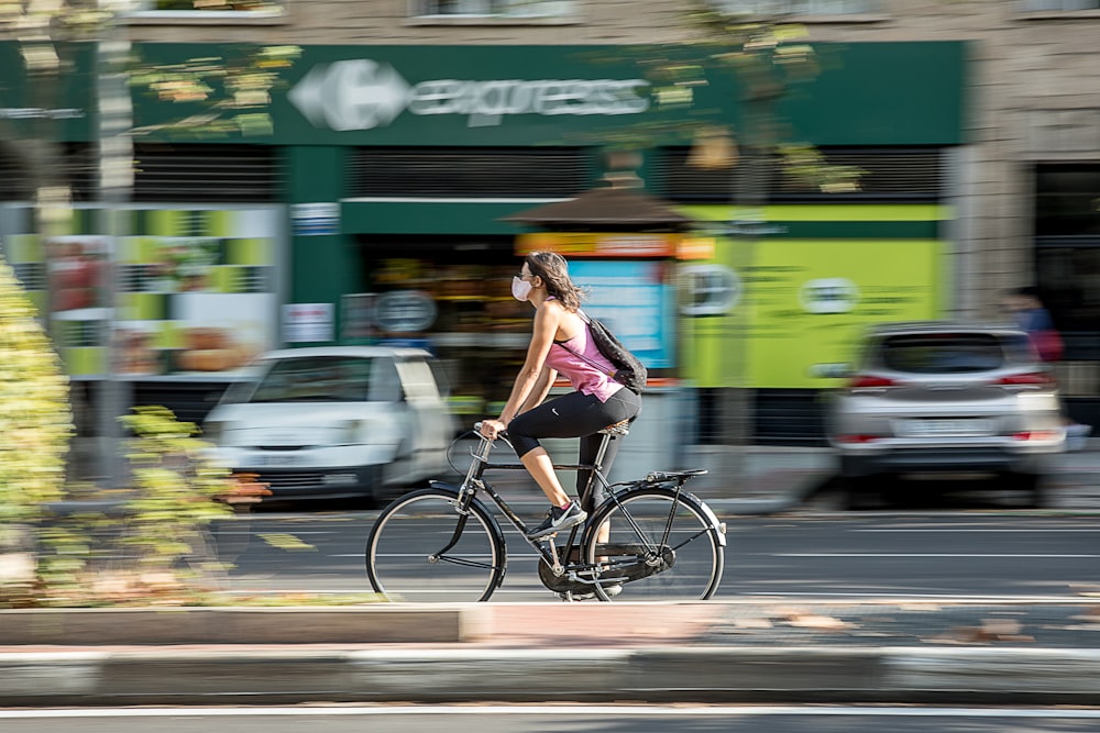 Donna in canotta viola e bianca che cavalca in bicicletta su strada durante il giorno