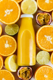 A bottle of orange juice is surrounded by an assortment of sliced citrus fruits, including oranges, lemons, limes, and passion fruits. The vibrant colors and fresh appearance create a visually appealing arrangement.