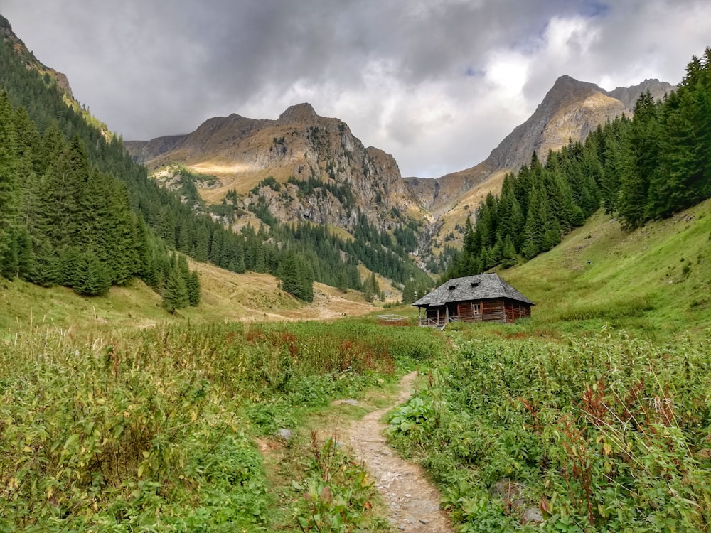 casa de madeira marrom no campo de grama verde perto da montanha sob nuvens brancas durante o dia