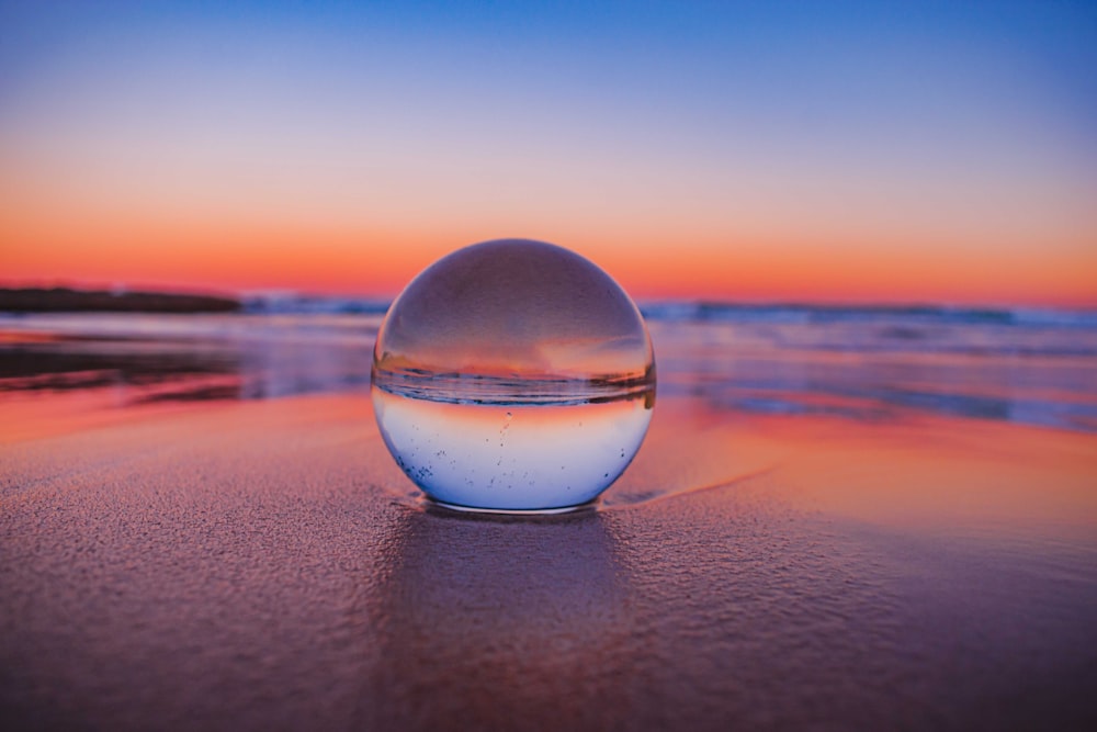 Boule de verre clair sur sable gris au coucher du soleil