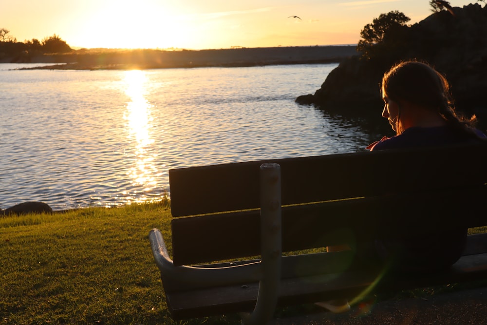 woman in black shirt sitting on brown wooden bench near body of water during daytime