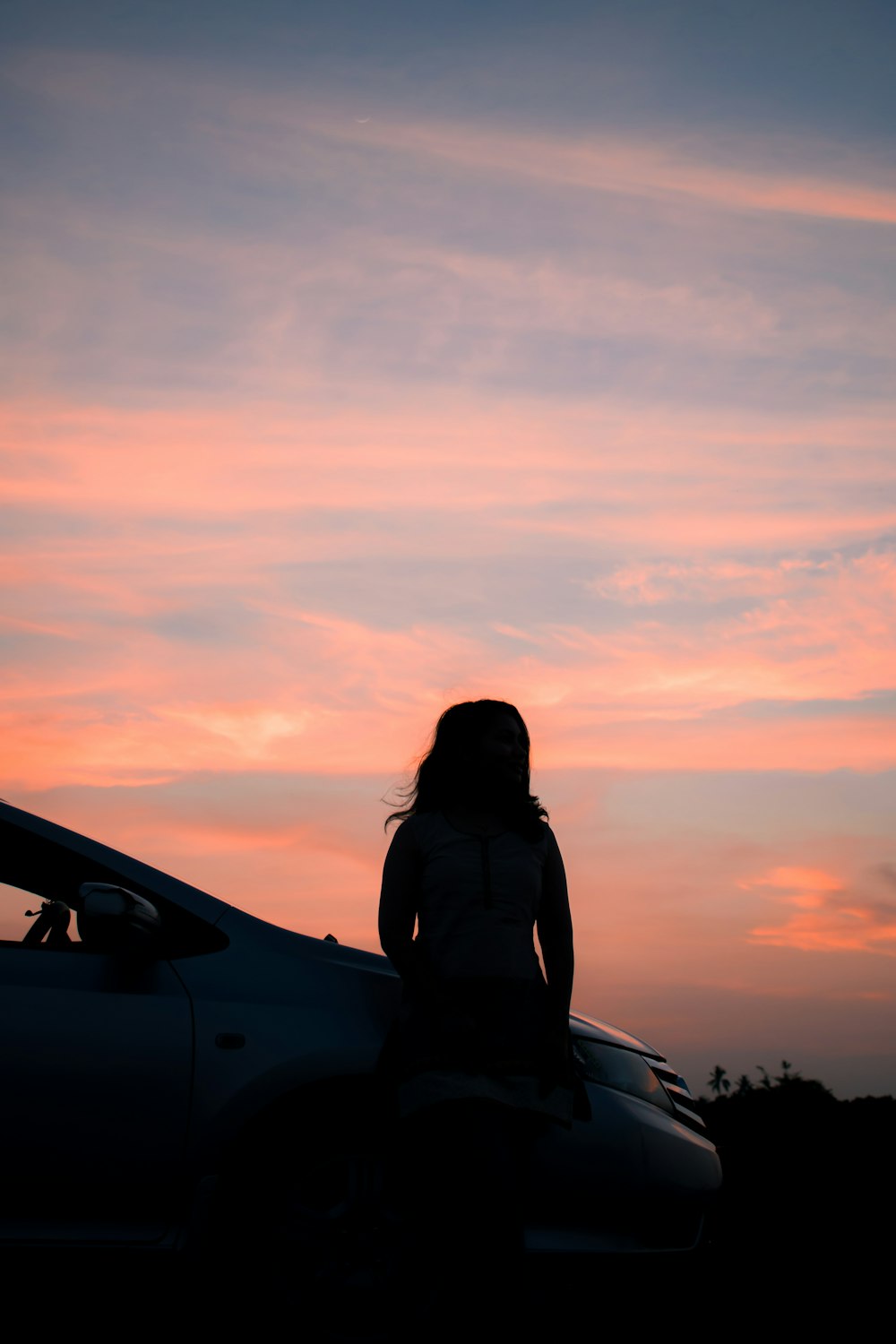 silhouette of woman sitting on car hood during sunset