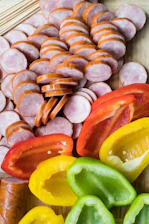 Close-up of sizzling Carolina sausage links topped with grilled onions, peppers, and jalapeños on a rustic wooden board.
