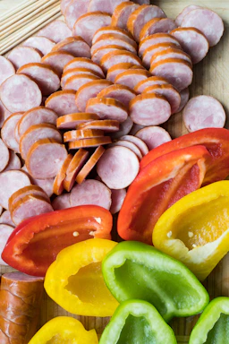 Close-up of sizzling Carolina sausage links topped with grilled onions, peppers, and jalapeños on a rustic wooden board.