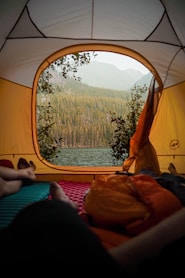 person lying on orange and white tent near body of water during daytime