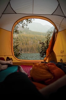 person lying on orange and white tent near body of water during daytime