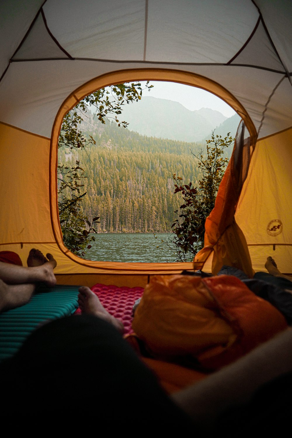 person lying on orange and white tent near body of water during daytime