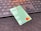 A green debit card with contactless payment symbol and a Mastercard logo is placed on a dark surface in front of a black computer keyboard. The keyboard keys have a soft orange backlight.