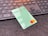 A green debit card with contactless payment symbol and a Mastercard logo is placed on a dark surface in front of a black computer keyboard. The keyboard keys have a soft orange backlight.