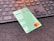 A green debit card with contactless payment symbol and a Mastercard logo is placed on a dark surface in front of a black computer keyboard. The keyboard keys have a soft orange backlight.