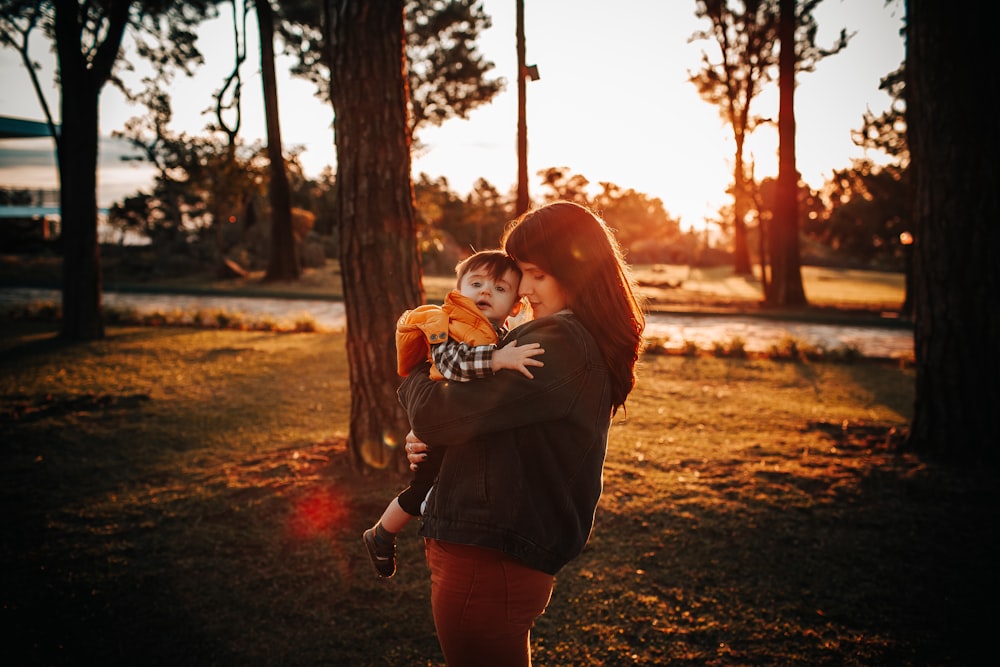 woman in brown long sleeve shirt carrying baby in brown jacket during daytime