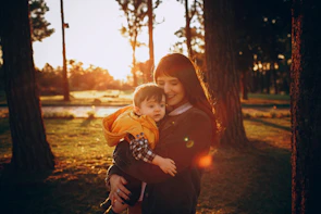 A mother and child holding hands, walking through a golden-lit park in the late afternoon.