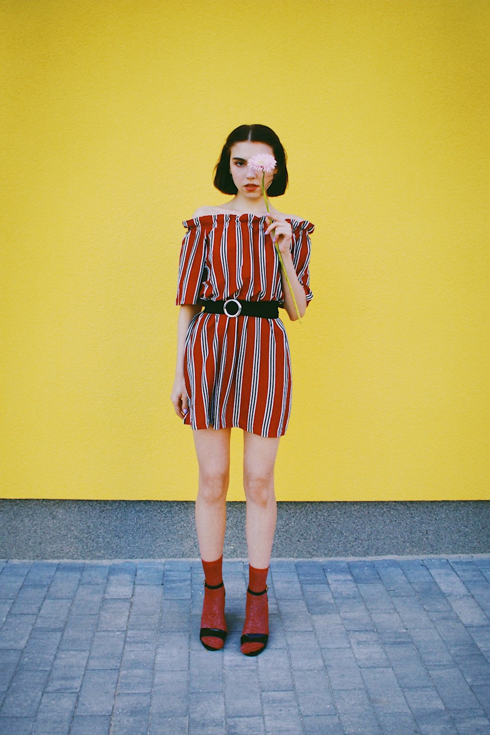 woman in white and red striped dress standing beside yellow painted wall