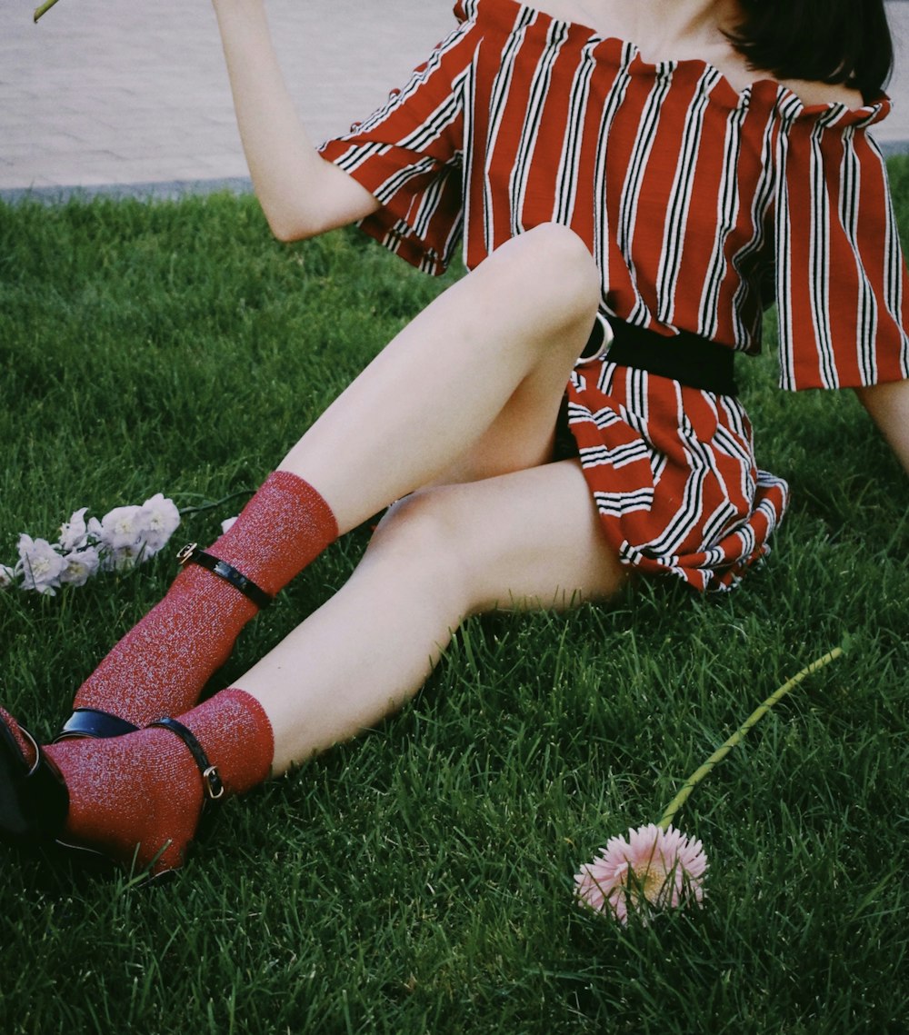 femme en robe à rayures rouges et blanches assise sur le champ d’herbe verte