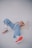 A person is lying on their back on a plain surface, wearing light blue jeans, a pink top, and white sneakers with orange soles. The pose is relaxed and casual, suggesting comfort.