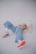 A person is lying on their back on a plain surface, wearing light blue jeans, a pink top, and white sneakers with orange soles. The pose is relaxed and casual, suggesting comfort.