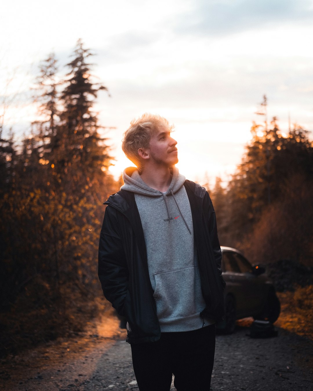 man in black zip up jacket standing near trees during daytime