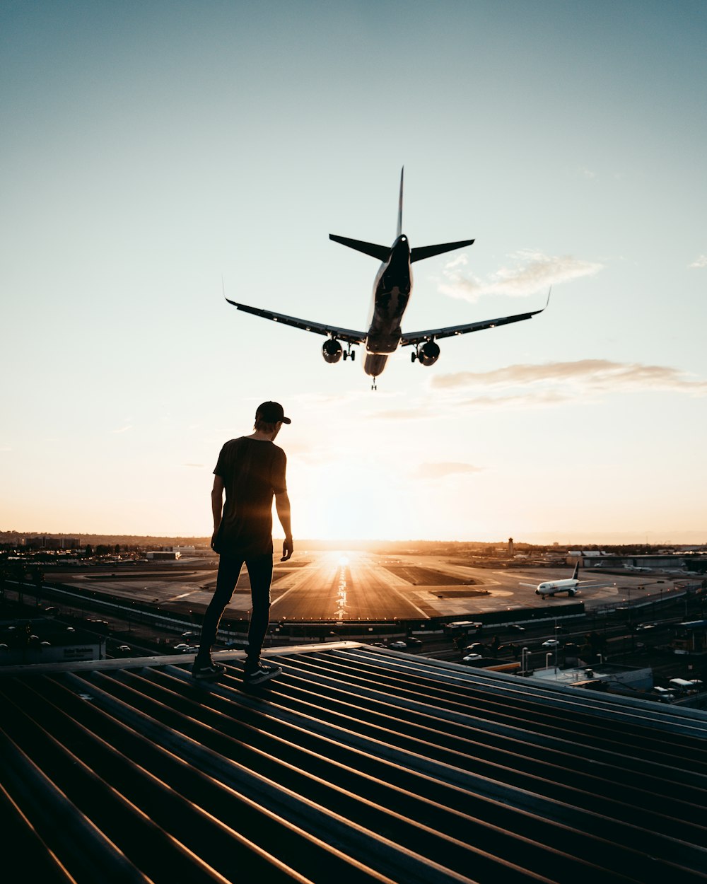 man standing on top of building looking at airplane in the sky during sunset