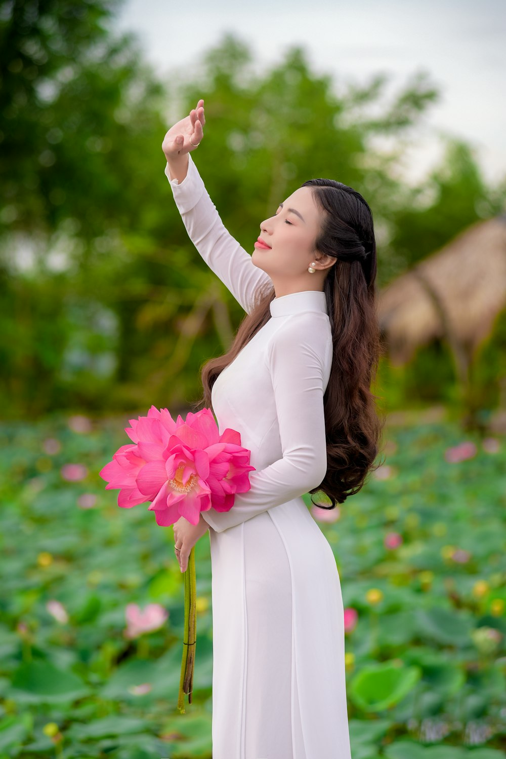 mulher no vestido branco da manga comprida que segura as flores cor-de-rosa