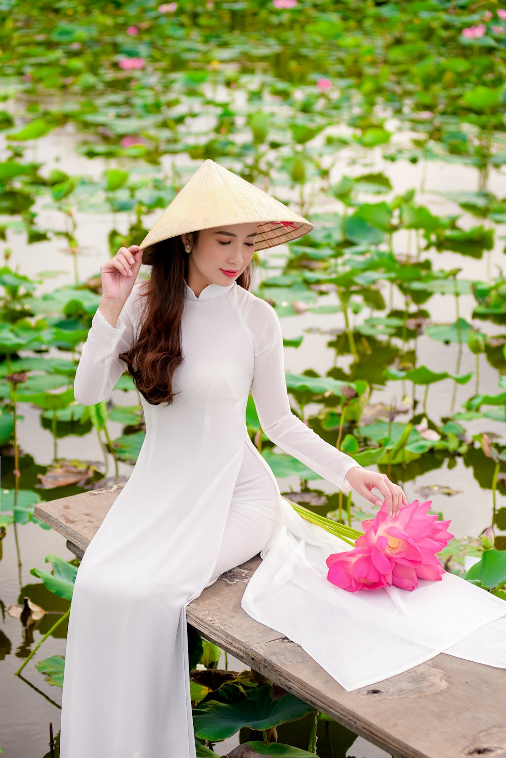 woman in white long sleeve dress wearing brown sun hat standing in front of green plants
