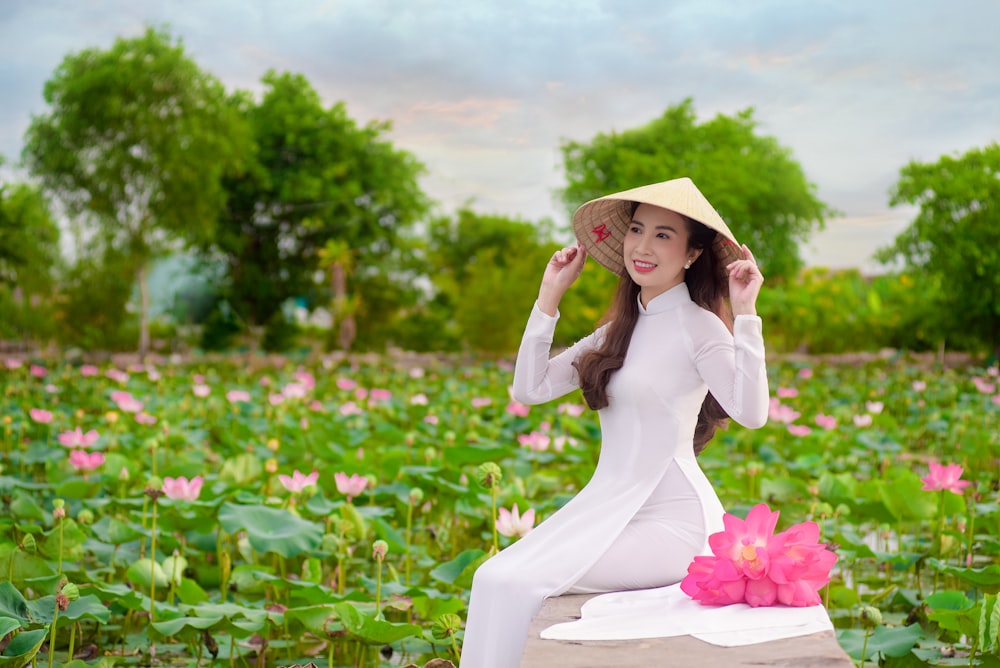 woman in white long sleeve dress wearing brown sun hat standing on flower field during daytime