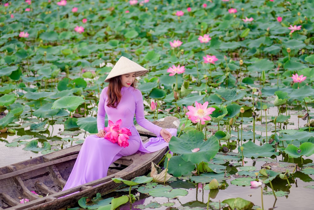 girl in pink dress sitting on brown wooden boat surrounded by green leaves during daytime