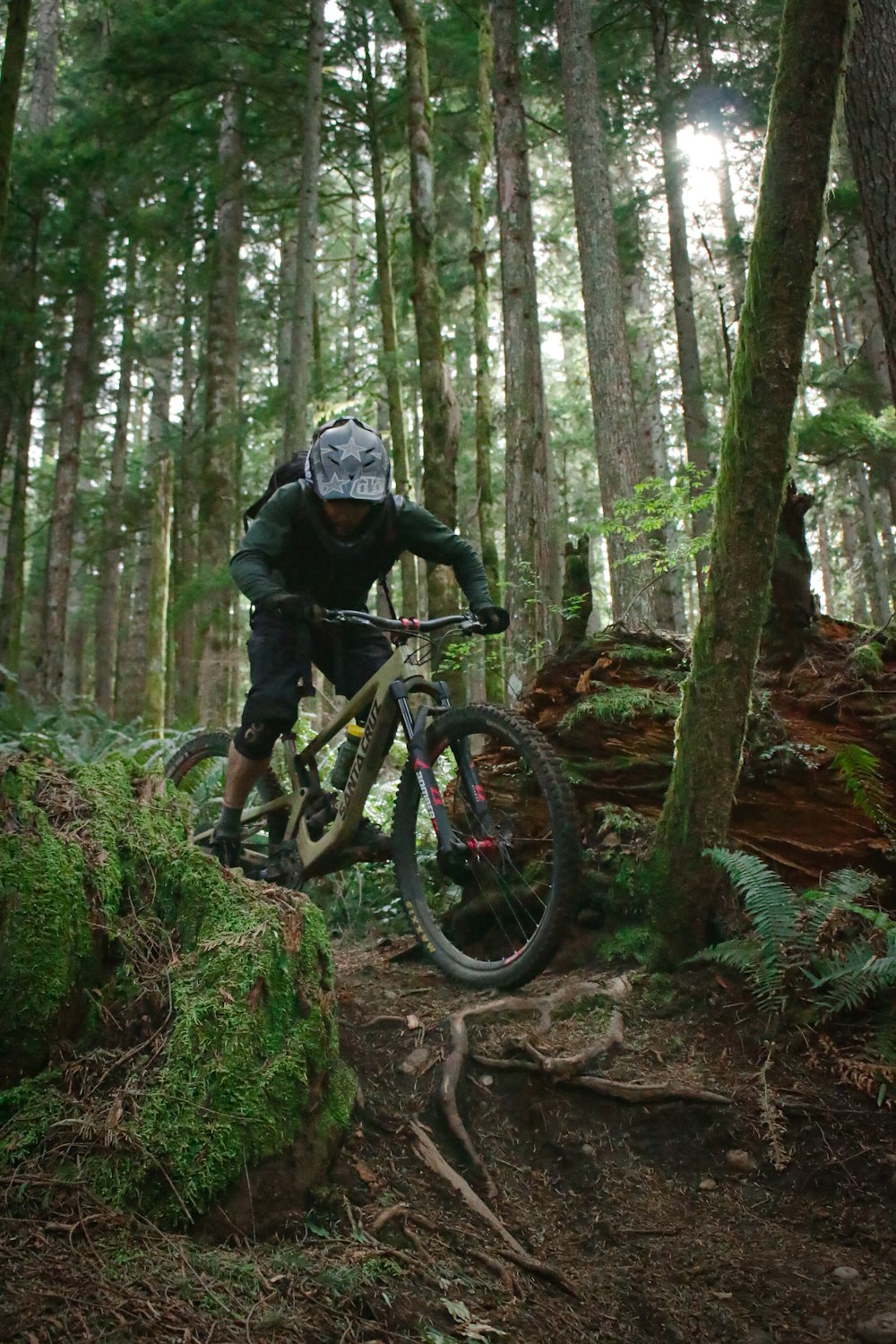 낮 동안 숲에서 검은 산악 자전거를 타는 검은 재킷을 입은 남자