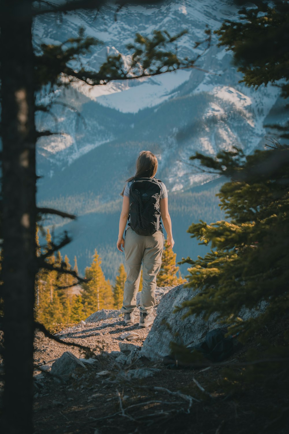 woman in black tank top and white pants standing on rocky ground near green trees during