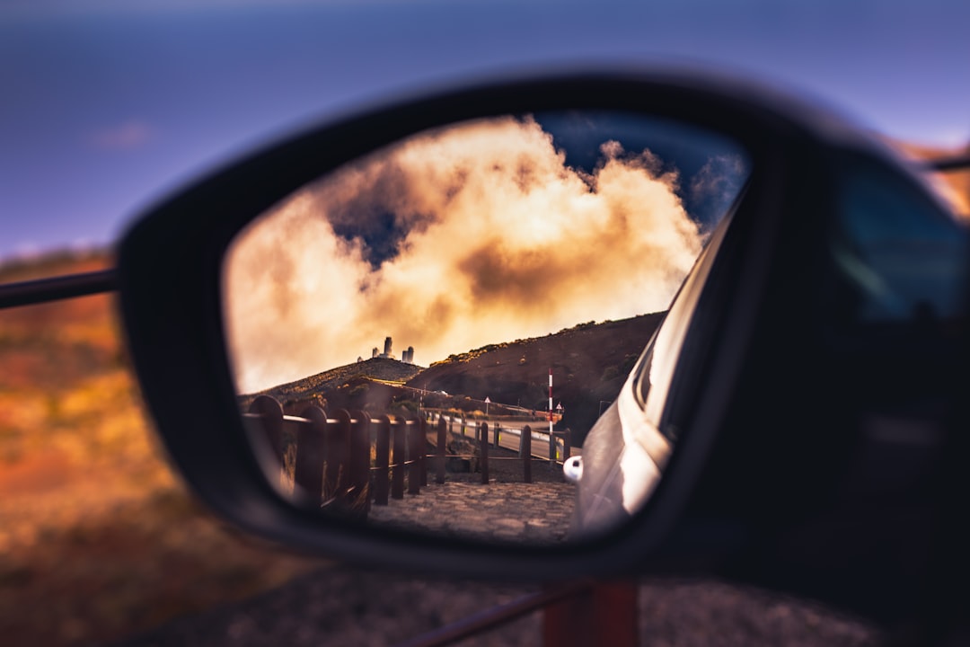 black car side mirror showing white and brown concrete building under cloudy sky during daytime