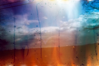 A photo with abstract elements, combining a serene landscape of a cloudy sky with artistic color distortions. Lines and spots in various colors overlay the scene, creating an ethereal effect.