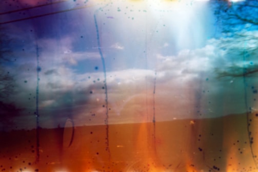 A photo with abstract elements, combining a serene landscape of a cloudy sky with artistic color distortions. Lines and spots in various colors overlay the scene, creating an ethereal effect.