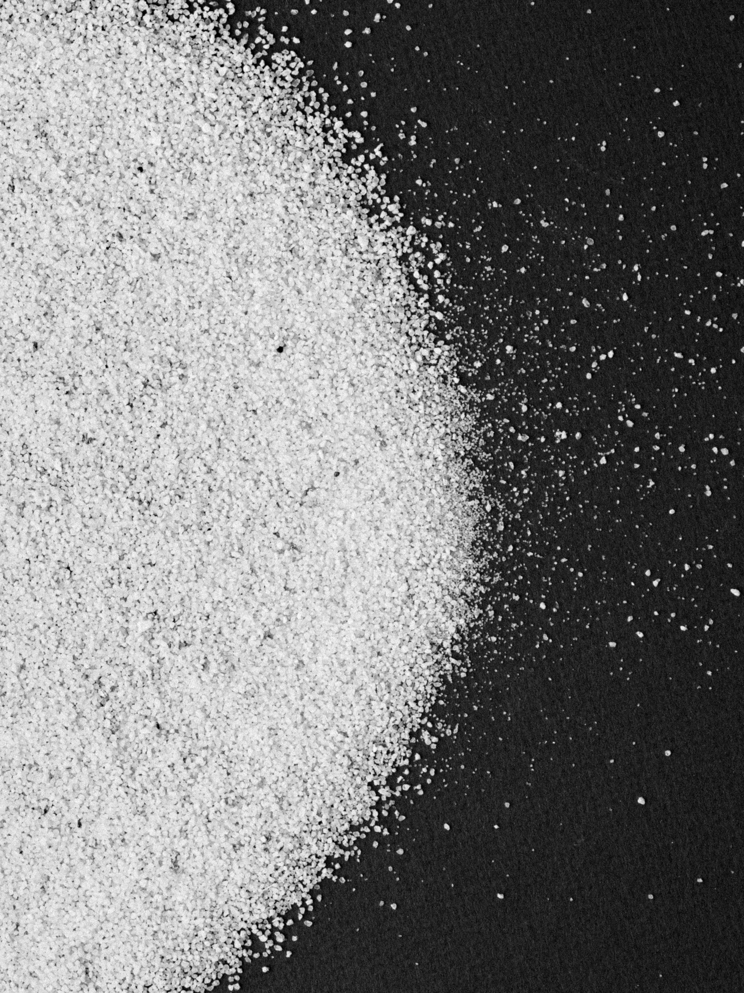 Black and white photo of white sand on a dark surface.