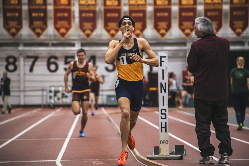 uomo in canotta blu che corre sul campo di atletica