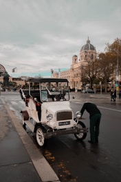 A mechanic inspecting a well-kept older car parked on a quiet village street.