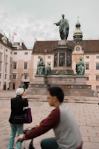 people walking on sidewalk near statue of man and woman during daytime