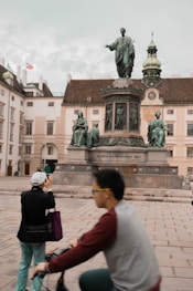 people walking on sidewalk near statue of man and woman during daytime
